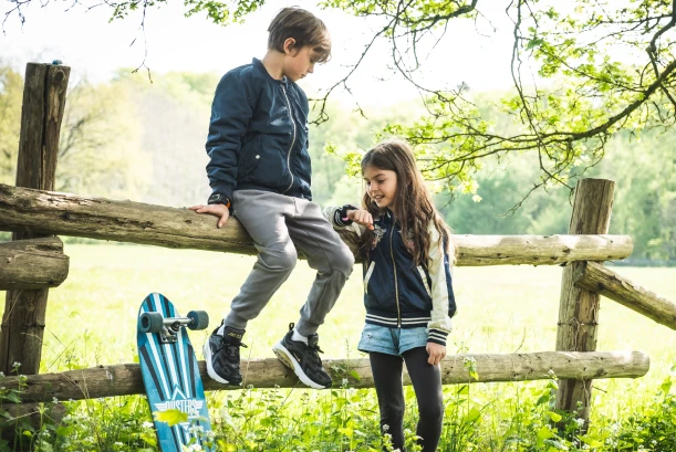 Kinder tragen in der Natur die Kids Watch XPLORA X6 am Handgelenk und schauen aus einem Zelt heraus.